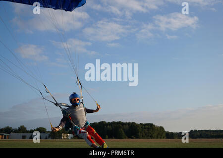 Skydiver under a dark blue little canopy of a parachute is landing on airfield, close-up. High-speed landing of a parachuter against the background of Stock Photo