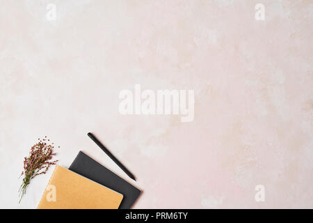 Feminine office concept. Top view of brown and black notebook with black pencil and wild flowers on rose background. Flat lay with copy space. Stock Photo