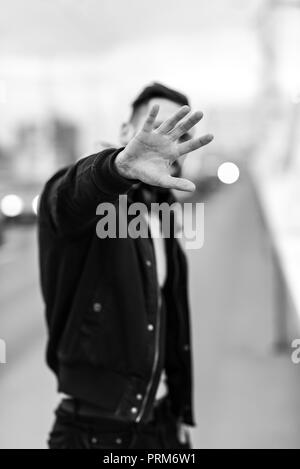 A young hipster man covering his face with his hand in an urban environment. Stock Photo