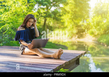 stressed woman using laptop computer on a wooden jetty Stock Photo