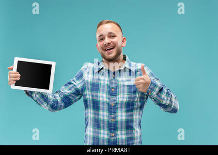 Studio picture of positive man isolated on blue background standing in casual clothes holding tablet and showing it blank screen with happy smile. He advising product or service. Stock Photo