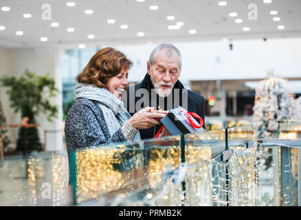 A senior woman giving a present to a man in shopping center at Christmas time. Stock Photo