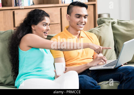 Smiling woman pointing on laptop screen showing something to her husband Stock Photo