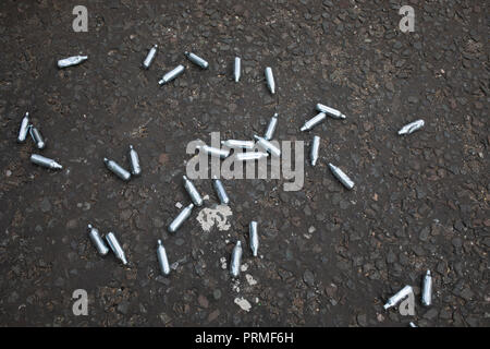 Empty cannisters of laughing gas lying on the street in East London, United Kingdom. Nitrous oxide, commonly known as laughing gas, nitrous, nitro, or NOS is now a very common 'legal high' used by young people. Nitrous oxide can cause analgesia, depersonalisation, derealisation, dizziness, euphoria, and some sound distortion. Inhalation of nitrous oxide for recreational use, with the purpose of causing euphoria and/or slight hallucinations, began as a phenomenon for the British upper class in 1799, known as 'laughing gas parties'. Stock Photo
