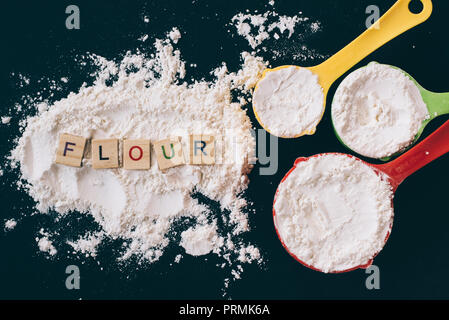 top view of a flour in a colorful measuring cup with FLOUR word on black background. concept of cooking,bakery and food ingredient Stock Photo