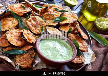 crispy Fried Eggplant Aubergine slices on a earthenware plate with yogurt parsley dipping in clay bowl on a rustic table with ingredients at the backg Stock Photo