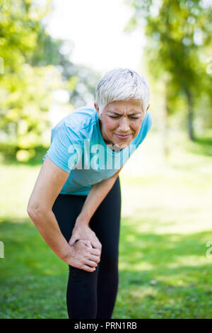 Senior sportswoman with knee pain standing in park on summer day Stock Photo