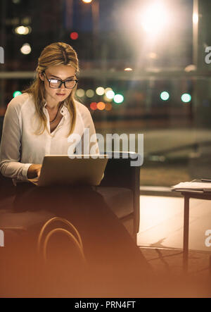 Young woman working late on laptop in office. Female business professional working over time in office to complete the project. Stock Photo