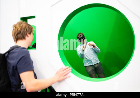 03 October 2018, Bremen: At the 69th International Astronautical Congress IAC, a young man looks through an opening into a green room where another man is trying out virtual reality glasses. Photo: Mohssen Assanimoghaddam/dpa Stock Photo
