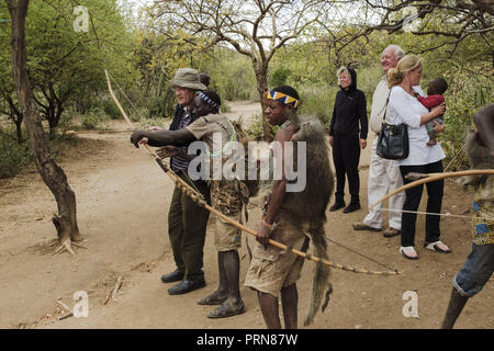 May 23, 2017 - Lake Eyasi, Ngorongoro district, Tanzania - American tourists visit one of the aproximately thirty Hadza camps. A white woman holds a black baby in her hands, while her husband tries to shoot an arrow on a distant tree. Each tourist group must pay a $20 fee for each visit. Small pocket money from tourism has become the main source of income for the Hadza people.The Hadza are one of the last remaining societies, which remain in the world, that survive purely from hunting and gathering. Very little has changed in the way the Hadza live their lives. But it has become increasingly h Stock Photo