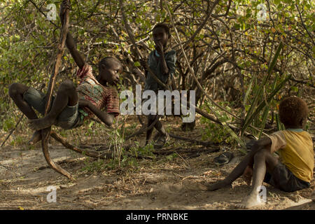 April 19, 2017 - Lake Eyasi, Ngorongoro district, Tanzania - Gorova (11), Babu (6) and his younger brother Dovu (5) play in the shade under some trees.The Hadza are one of the last remaining societies, which remain in the world, that survive purely from hunting and gathering. Very little has changed in the way the Hadza live their lives. But it has become increasingly harder for them to pursue the Hadza way of life. Either the Hadza will find a way to secure their land-rights to have access to unpolluted water springs and wild animals, or the Hadzabe lifestyle will disappear, with the majority Stock Photo