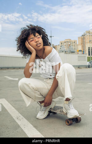 beautiful young african american woman crouching on skateboard and looking away on street Stock Photo