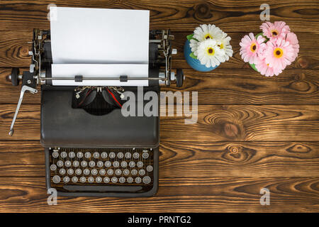 Overhead view of vintage metal typewriter next to blue and pink flowers sitting on wooden plank table Stock Photo