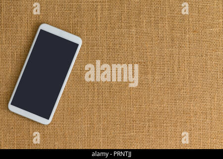 One white smart phone sitting on surface made up of light brown crisscrossed thread. Includes copy space. Stock Photo