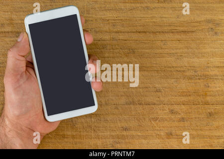 Overhead view of unidentified man using hand to holding smart phone over scratched wooden background Stock Photo