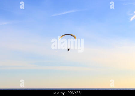 Single Powered paragliders with red and yellow canopy above a blue sea and soft clouds Stock Photo