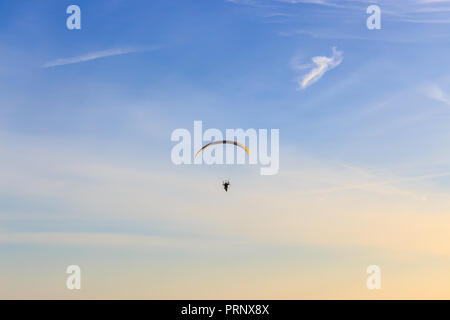 Single Powered paraglider with red and yellow canopy in blue sky and soft wispy clouds Stock Photo