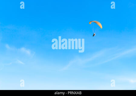 Single Powered paraglider with red and yellow canopy in blue sky and soft wispy clouds Stock Photo