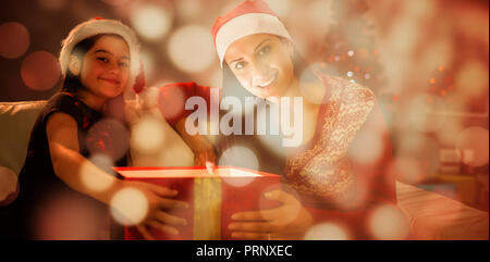 Composite image of festive mother and daughter opening a glowing christmas gift Stock Photo