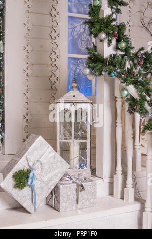 Winter exterior of a country house with Christmas decorations. wooden vintage porch.house decorated and lighted for Christmas and for New Year Eve. Big white lantern, gift boxes and balls. Stock Photo