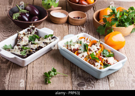 Stuffed eggplants with sun dried tomatoes,   bell peppers with minced meat, baked vegetables with mozzarella cheese on top in ceramic dishes on rustic Stock Photo