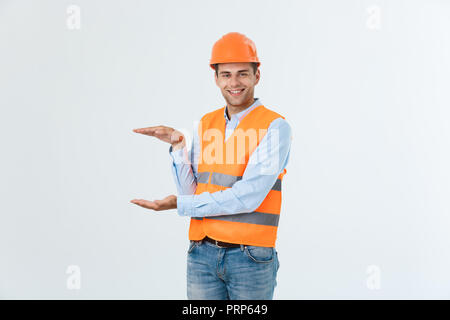 Happy beard engineer holding hand on side and explaining something, guy wearing caro shirt and jeans with yellow vest and orange helmet, isolated on white background Stock Photo