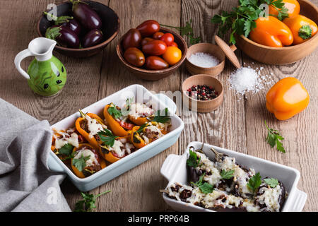 Stuffed eggplants with sun dried tomatoes,   bell peppers with minced meat, baked vegetables with mozzarella cheese on top in ceramic dishes on rustic Stock Photo