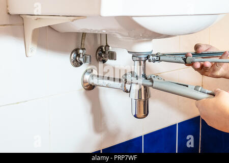 plumber fixes sink siphon by two pipe-wrenches in bathroom Stock Photo