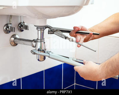 man adjusts two old pipe-wrenches to install a sink siphon in bathroom Stock Photo