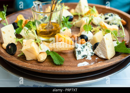 various kinds of cheeses with nuts and honey on wooden plate in restaurant Stock Photo