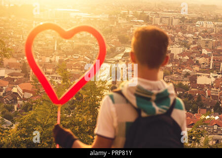 back of blurred boy holding heart balloon in front of city of Prizren in the evening sunshine Stock Photo