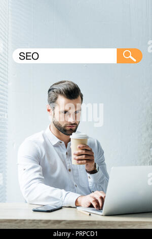 concentrated developer holding coffee to go while working with laptop with SEO search bar Stock Photo