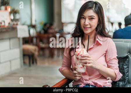 young woman holding strawberry frappe with whipped cream in the cafe Stock Photo