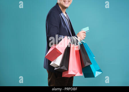 Close up of man  in suit holding credit card with shopping bags , isolated on light blue background . Stock Photo