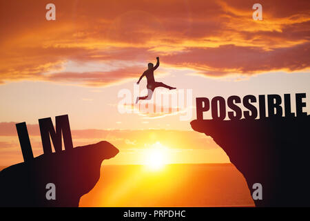 Man jumping over impossible or possible over cliff on sunset background Stock Photo
