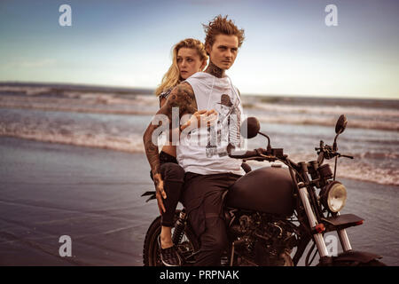 attractive girlfriend hugging boyfriend from back on motorcycle on ocean beach Stock Photo