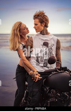 couple holding hands and looking at each other near motorcycle on ocean beach Stock Photo