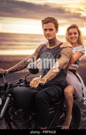 young heterosexual couple sitting on motorcycle and looking at camera at beach Stock Photo