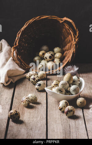 organic quail eggs in wicker basket and feather on wooden table Stock Photo