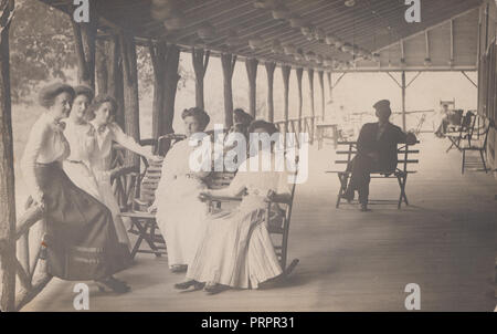 * Vintage Photograph of a Lady Sat In a Rocking Chair on a Porch In The Company of Her Female Companions or Family Stock Photo