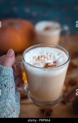 Close-up of hand holding pumpkin spice latte in glass cup, on wooden background Stock Photo