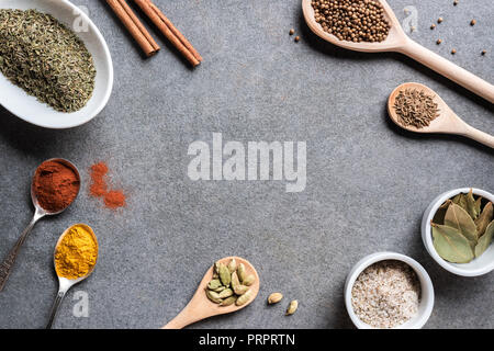 various aromatic dried seasonings in bowls and spoons on grey background Stock Photo