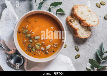 top view of bowl with pumpkin cream soup with seeds and bread on table Stock Photo