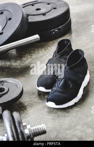 close-up shot of sneakers and weight plates on concrete surface Stock Photo