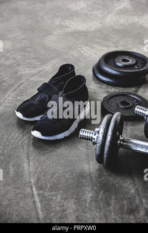 close-up shot of dumbbells with weight plates and sneakers on concrete floor Stock Photo