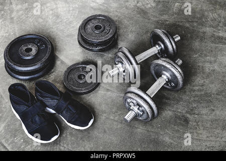 close-up shot of dumbbells with weight plates and sneakers on concrete surface Stock Photo