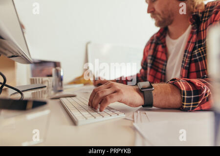 Hands of man typing on keyboard and making notes in office. Computer programmer working at the desk. Stock Photo