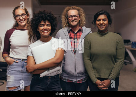 Portrait of young people standing together at startup office looking at camera and smiling. Confident team to IT professionals. Stock Photo