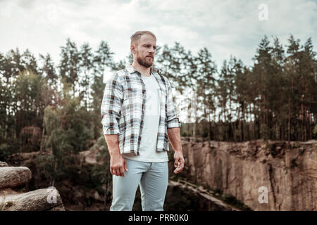 Bearded man wearing jeans and squared shirt standing in the rocky surroundings Stock Photo