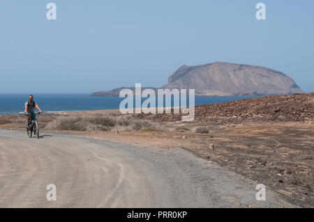 Lanzarote, Canary Islands: boy biking on the dirt road to the beach Playa de Las Conchas in the north of La Graciosa, main archipelago island Chinijo Stock Photo